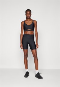 Top desportivo preto com design recortado, combinado com calções de ciclismo pretos e combinados. Ambos feitos de tecido liso, elástico e com um estilo ajustado.