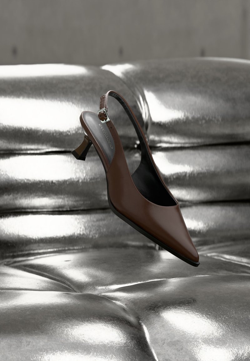 Chaussure à talon haut à bride arrière en cuir brun reposant sur une surface capitonnée métallique argentée brillante.