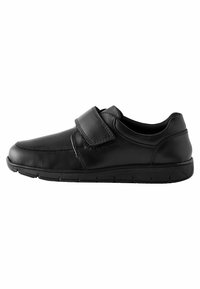 Chaussure en cuir noir avec un bout arrondi, bande auto-agrippante ajustable et une semelle texturée. Présente des détails de couture le long de la tige.
