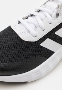 Chaussure de sport noir et blanc avec une tige en maille, des lacets plats et une semelle en caoutchouc texturée avec des rainures horizontales distinctes.
