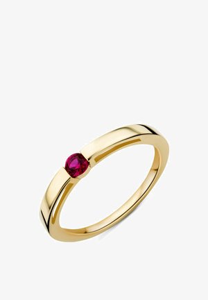 Auksinis žiedas su vienu apvaliu raudonu brangakmeniu, pritvirtintu modernioje, minimalistinėje juostoje ant balto fono.