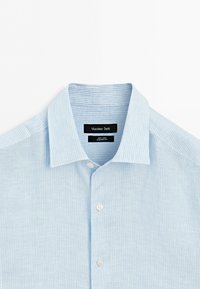 Chemise en lin bleu clair avec de fines rayures blanches verticales, boutonnée sur le devant, col classique et une étiquette noire portant le nom Massimo Dutti.
