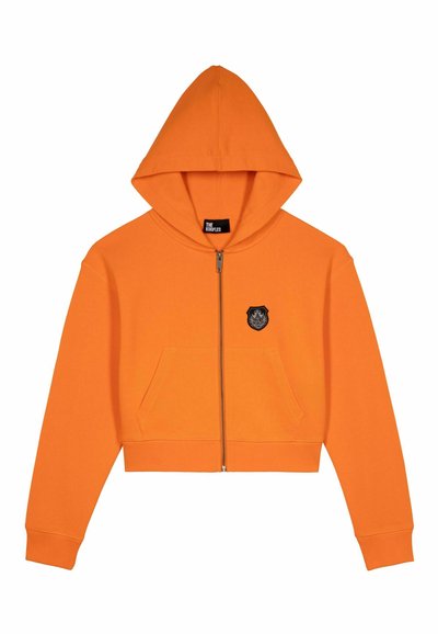 Felpa arancione corta con zip frontale, due tasche e un patch emblema nero sul petto. Tessuto liscio e cappuccio regolabile.
