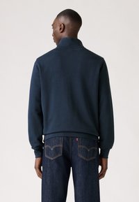 Marineblauwe sweatshirt met een hoge kraag, gemaakt van zachte stof. Heeft ribgebreide manchetten en een aansluitende zoom, gecombineerd met donkerdenim jeans.