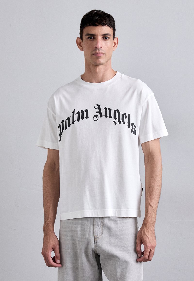 Hvit bomulls t-skjorte med svart "Palm Angels" tekst i en buet stil, korte ermer og en avslappet passform. Teksturen ser myk ut.
