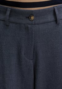 Dunkelblaue maßgeschneiderte Hose aus strukturiertem Stoff mit einem einzelnen Knopfverschluss und einer versteckten Vorderseite.