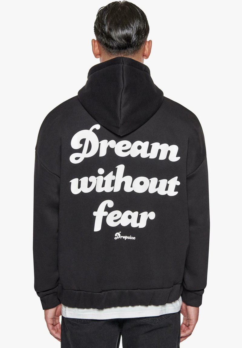 Schwarzer Kapuzenpullover mit Kordelzug und weißem Text "Traume ohne Angst" auf dem Rücken sowie einem gerippten Saum und Bündchen.