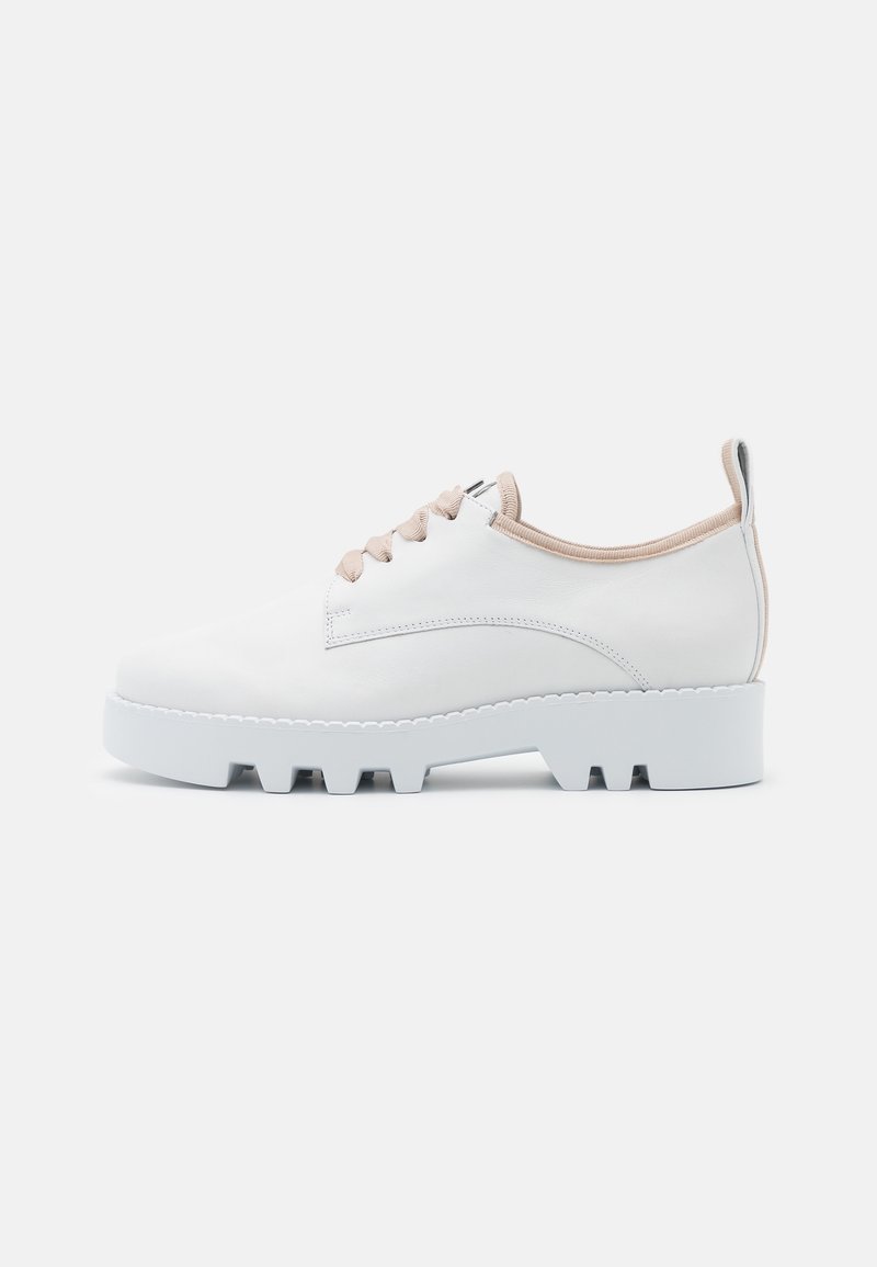 Baskets en cuir blanc avec des lacets beige, une tige texturée et une semelle blanche épaisse présentant des rainures peu profondes. Design minimaliste et coutures discrètes.