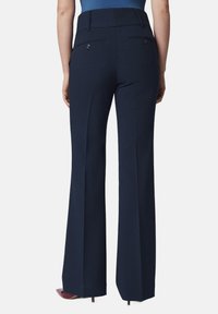 Granatowe spodnie w typie dzwonów o gładkiej teksturze, z dwoma tylnymi kieszeniami i wysokim stanem. Czyste linie biegną od bioder do dołu.