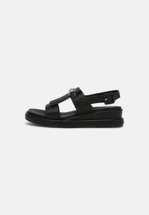 Sandalia negra con parte superior de cuero texturizado, correa ajustable en el tobillo y suela de cuña para mayor altura y comodidad.