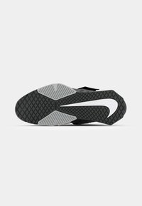 Semelle de chaussure de sport noire avec un motif de semelle texturé, présentant un swoosh Nike blanc et des accents gris.