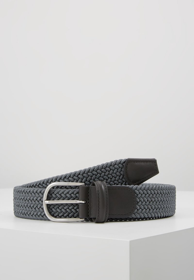 Ceinture en tissu tressé gris avec des accents en cuir noir et une boucle en métal argenté, enroulée sur une surface blanche.