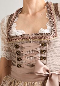 Gros plan sur un corsage traditional beige de dirndl avec une blouse en dentelle, un laçage décoratif, une broderie et un grand nœud noué à la taille.