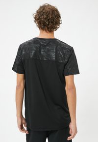 Sort t-shirt med en struktureret, camouflage-mønstret yoke, med korte ærmer og lige snit, lavet af letvægtsstof.