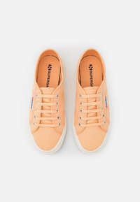 Broskvové plátěné tenisky s bílými gumovými podrážkami, kulatou špičkou a šněrováním na pět dírek. Na boku mají logo.