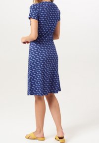 Modré šaty s motivem velryb, krátké rukávy a rozevlátá sukně. Nosí se s žlutými sandály, které mají hladkou látku a uvolněný design.