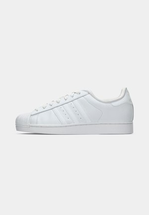 White leather sneaker with a textured rubber toe cap, three side stripes, and a cushioned collar. Flat white laces and a minimal design.