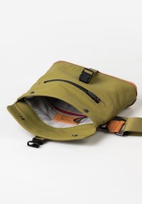 Olivgrüne Tasche mit einer strukturierten Außenseite, schwarzem Reißverschluss und Akzenten aus braunem Leder. Verfügt über einen verstellbaren Tragriemen und ein gefüttertes Innere mit Taschen.