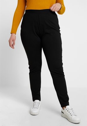Czarne, dopasowane spodnie z elastycznego materiału o gładkiej fakturze i elastycznym pasie. Połączone z białymi trampkami i żółtą bluzką.