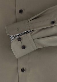 Olijfgroen overhemd met lange mouwen, voorzien van zwarte knopen, een contrasterende, gemusterde binnenkant en een gladde, textuurstof.