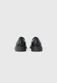 Pair of black leather dress shoes with low stacked heels shown from the back on a plain white background.