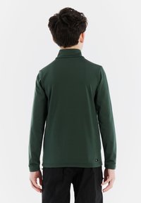 Pullover lungo a maniche lunghe di colore verde scuro con colletto alto. Tessuto liscio e elasticizzato con vestibilità regolare. Etichetta nera sul lato vicino all'orlo.