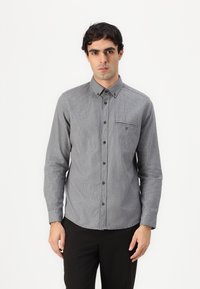 Gray plaid button-up shirt with long sleeves, featuring a chest pocket and brown buttons, made of a textured fabric. Worn with black pants.