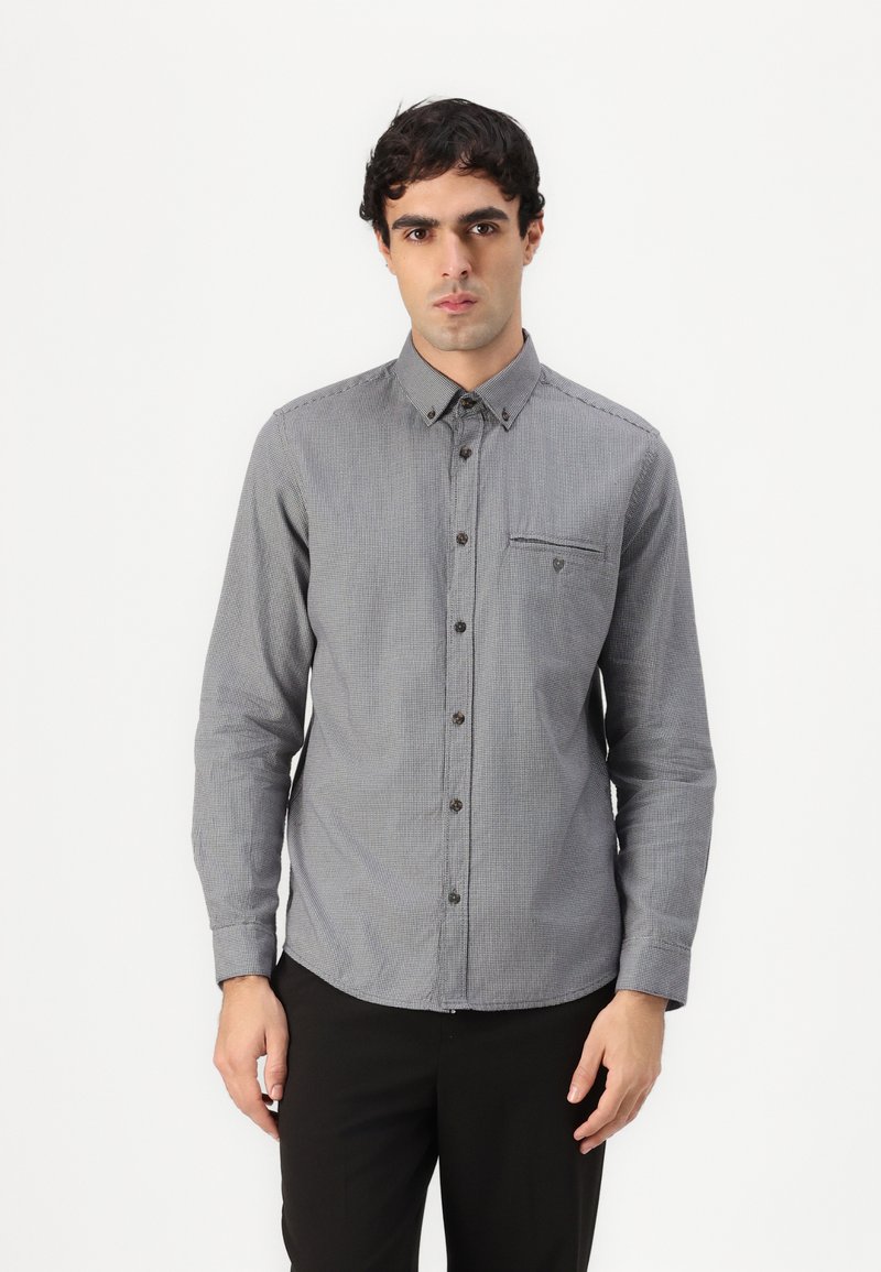 Gray plaid button-up shirt with long sleeves, featuring a chest pocket and brown buttons, made of a textured fabric. Worn with black pants.