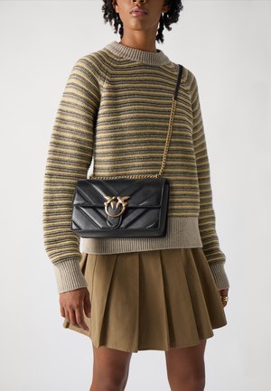 Borsa a tracolla in pelle nera con design trapuntato, hardware in tonalità oro e tracolla a catena, posizionata su un maglione a righe e una gonna.