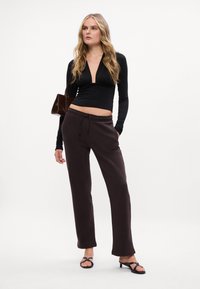 Melnas garās piedurknes tops ar dziļu V-veida izgriezumu, kombinēts ar tumši brūnām sporta biksēm ar pagarinātu jostasvietu. Vienkārša, pieguļoša stila un plakanas čības.