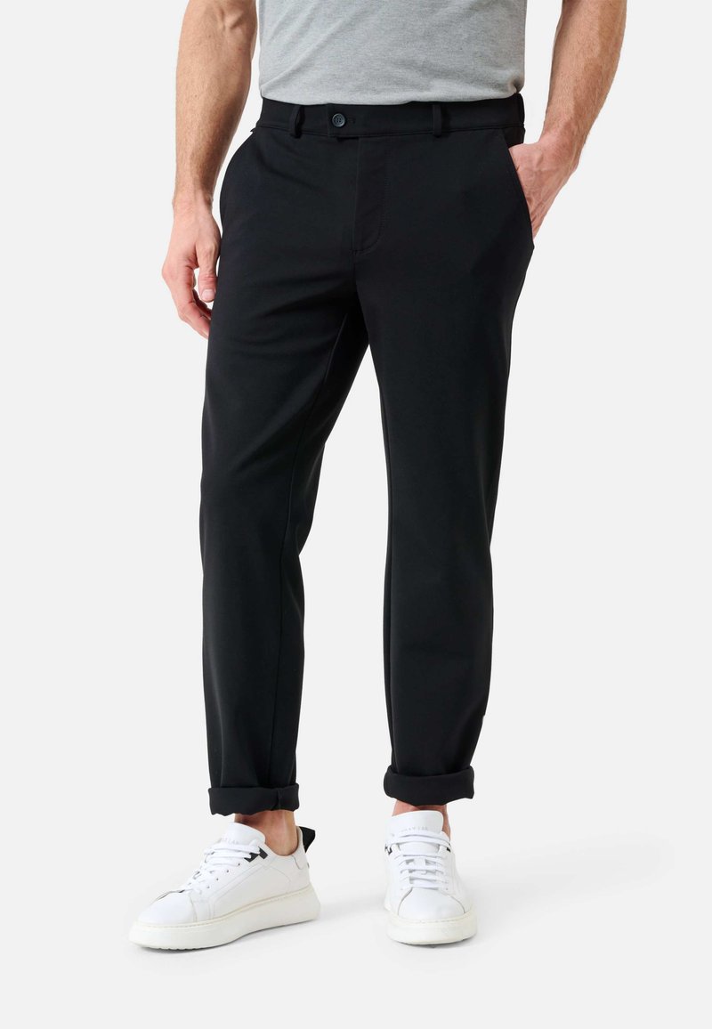 Pantalons noirs en tissu doux, avec une coupe droite, poches avant et ourlets retroussés aux chevilles, assortis à des baskets blanches.