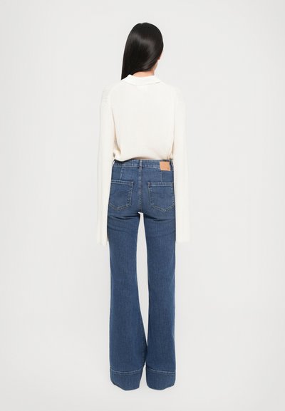 Jeans blu a zampa d'elefante con vita alta, cinque tasche e patch in pelle sul retro. Abbinati a un top cream a maniche lunghe e a coste.