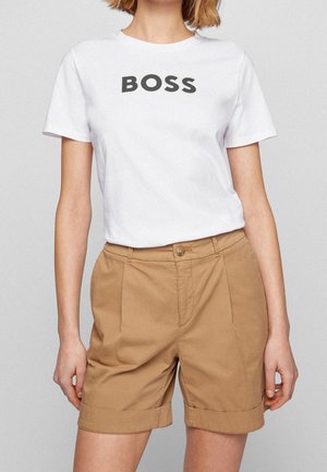 Witte katoenen t-shirt met het woord "BOSS" in vetgedrukte zwarte letters, gecombineerd met beige opgerolde shorts van een lichtgewicht stof.