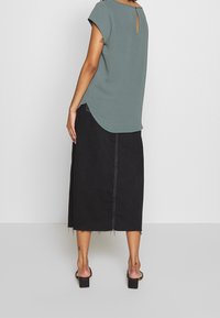 Top grigio a maniche corte con dettaglio a chiave sul retro, abbinato a una gonna midi in denim nera con orlo sfilacciato e accenti di cucitura bianca.