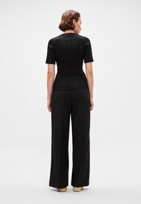 Juodas raštuotas megztinis trumpomis rankovėmis, prigludusi silueto, apvaliu iškirpimu, derinamas su didelio liemens, plačiomis juodomis kelnėmis.