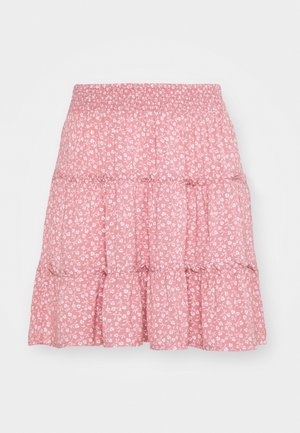 Jupe rose à volants avec taille élastique, ornée d'un petit motif floral blanc sur un fond uni.