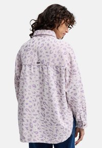 Jasnofioletowa koszula z korduroyu o luźnym kroju, z wzorem w panterę, z guzikami przy mankietach i zaokrąglonym dołem.