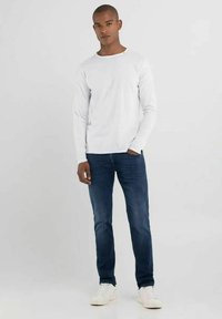 Camicia bianca a maniche lunghe, jeans blu e sneakers bianche. Design semplice, forma aderente, texture liscia e senza motivi o accenti visibili.