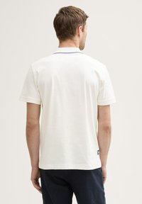 Polo shirt bianco a maniche corte con colletto classico, caratterizzato da un accento blu sul colletto e da un piccolo etichetta del marchio all'anca.