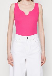 Fuksjowy bodysuit bez rękawów z dekoltem w kształcie litery V, w połączeniu z białymi dżinsami z wysokim stanem. Miękki, elastyczny materiał o dopasowanym kroju.