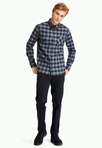 Grå och svart rutiga skjorta med långa ärmar, knäppt upp, med krage och en bröstficka; kombinerad med mörka byxor och svarta skor.