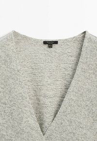 Light gray knitted sweater featuring a deep V-neckline, soft texture, and subtle pattern with a tag visible at the center back.
