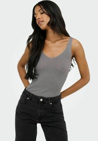 Top de tirantes ancho en color gris, con textura acanalada y escote en forma de V; combinado con unos vaqueros negros de talle alto, que acentúan una silueta ajustada.