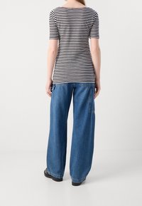 Camiseta de rayas con un cuello ancho y mangas cortas, combinada con jeans azul índigo de pierna ancha y suelta, con un bolsillo parche. Zapatos negros.