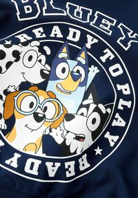 Námornícky modrá látka s kreslenými postavičkami psov s veľkými očami, okuliarmi a hravými výrazmi, okolo textu "PRIPRAVENÍ NA HRU".