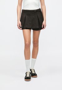 Brown pleated shorts with a belt loop and button detail. Material appears textured. Worn with white knee-high socks and black shoes.