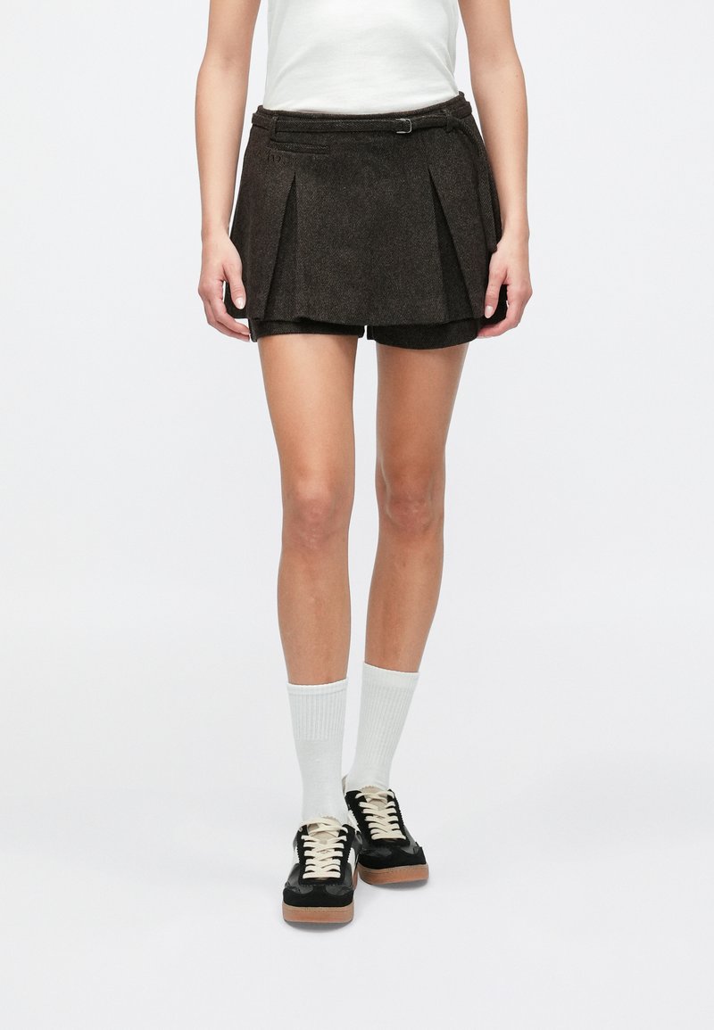 Brown pleated shorts with a belt loop and button detail. Material appears textured. Worn with white knee-high socks and black shoes.