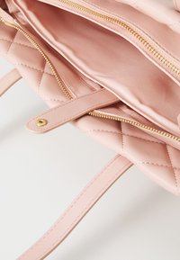 Rožinė siuvinėta rankinė su auksine užtrauktuko detalėmis, turinti sklandžią, odos panašią išorinę dalį ir erdvų vidų. Įtrauktos dvi rankenos.