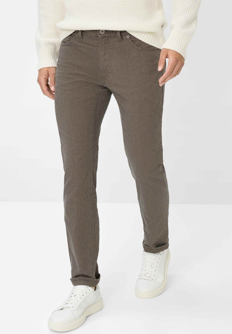 Pantaloni marroni slim-fit realizzati in tessuto testurizzato, dotati di tasche frontali e chiusura con bottone, abbinati a sneakers bianche.