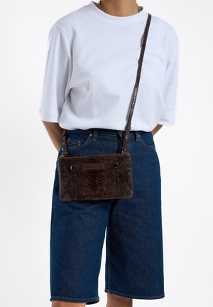 Sac bandoulière en imprimé serpent marron texturé, forme rectangulaire, doté d'une sangle lisse et d'une quincaillerie minimaliste, porté par une personne.